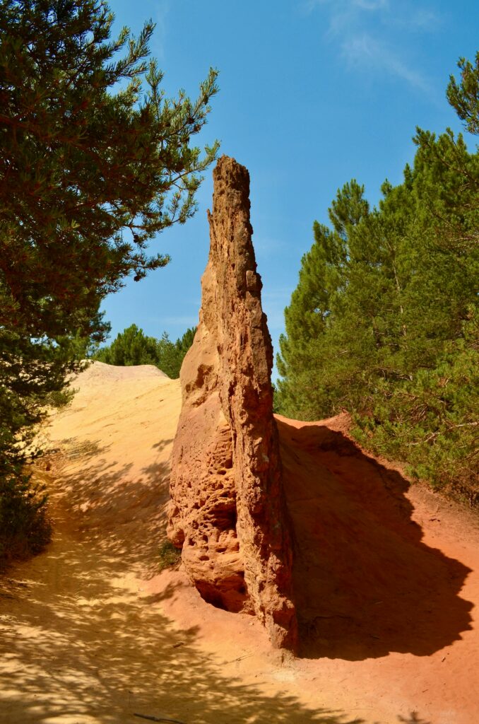 Captivating red ocher rock formation surrounded by lush green forest in Rustrel, Provence, France.